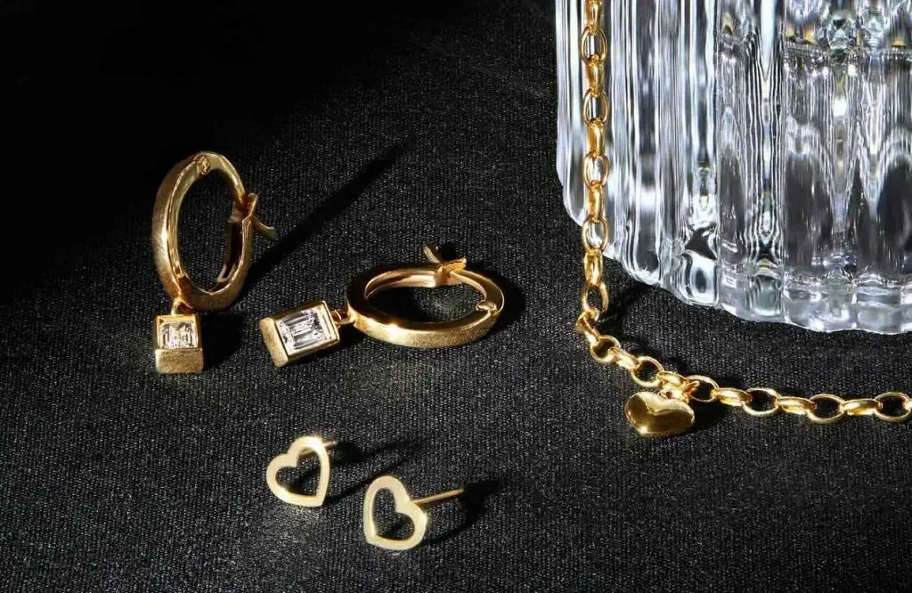 Elegant gold jewelry featuring hoops, earrings, and chain with heart charms, perfect for gifting or special occasions.