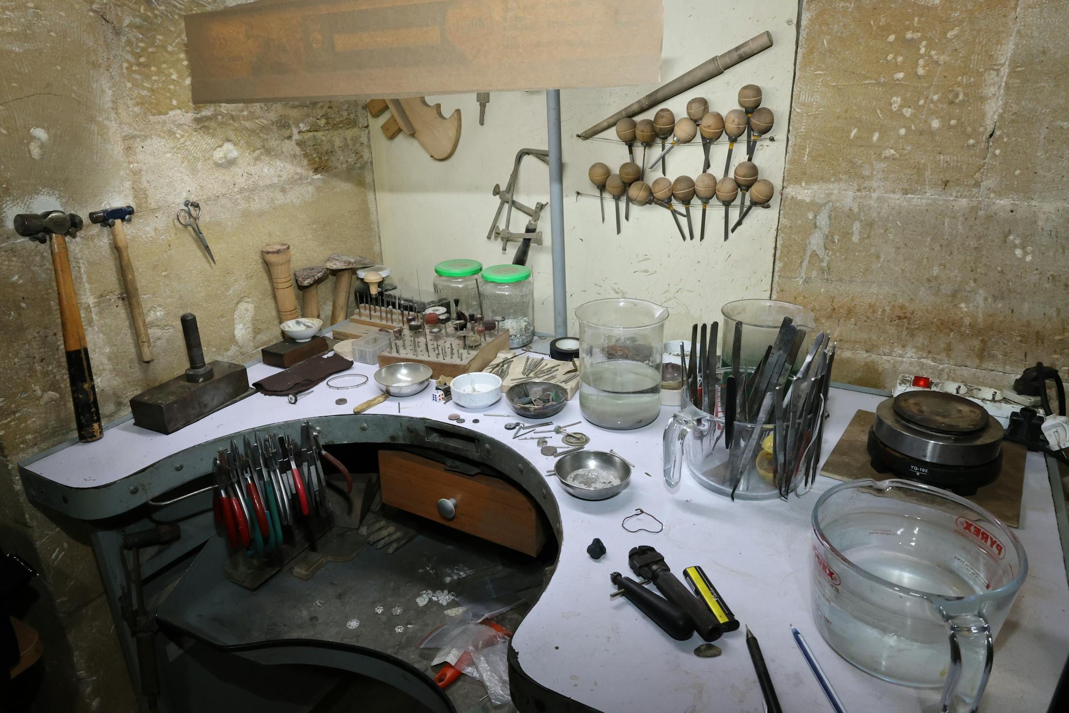 Small jewellery studio workspace with tools, finished pieces and a laptop